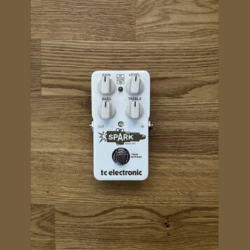Bílý kytarový efekt s nápisy GAIN, LEVEL, BASS a TREBLE u ovládacích knoflíků. Uprostřed je přepínač s označením FAT, CLEAN a MID. Na spodní části je…