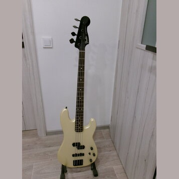 Elektrická basová kytara v krémové barvě s hnědým hmatníkem. Na hlavě nástroje je viditelné logo Fender. Tělo má dva snímače a čtyři ovládací knoflík…
