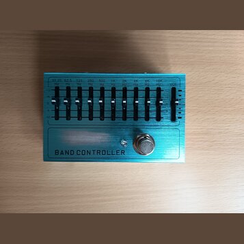 Modrý ekvalizér s kovovým povrchem a nápisem BAND CONTROLLER. Zařízení obsahuje 10 posuvníků s označením frekvencí od 31.25 Hz do 16K Hz a jeden posu…