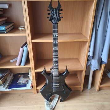 Černá elektrická kytara s výrazně hranatým tvarem těla a hlavou ve tvaru rohu. Na hlavě je bílý nápis B.C. Rich. Hmatník obsahuje bílé ornamentální v…