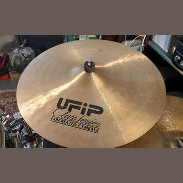 Zlatavý kovový činel s černým logem a nápisy UFIP, Class Series a EARCREATED CYMBALS. V centru je umístěna černá plstěná podložka s kovovým šroubem.…