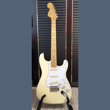 Krémově bílá elektrická kytara s jasným javorovým hnedlem krku a hmatníkem. Na hlavě je viditelné logo Fender. Kytara má tři snímače, bílý pickguard…