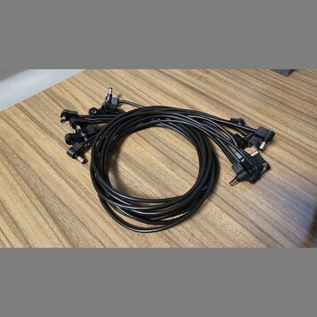 Na fotografii je černý vícežilový kabel s několika koncovými konektory typu jack. Kabel je svinutý do kruhu a položen na dřevěném povrchu. Na viditel…