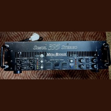 Černý kytarový zesilovač v rackovém provedení s úchyty po stranách. Na horním panelu je bílý nápis Simul. 395 STEREO a pod ním logo MESA/BOOGIE. Upro…