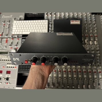 Černý rackový kompresor a limiter s kovovým předním panelem. Vlevo je logo DBR, vpravo nápis COMPRESSOR LIMITER dB. Přístroj má čtyři černé otočné kn…
