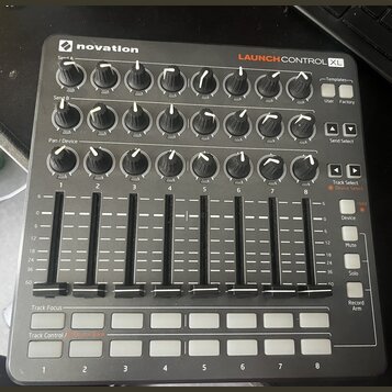 Černý MIDI kontrolér značky novation s nápisem LAUNCH CONTROL XL. Zařízení obsahuje tři řady otočných knoflíků s bílými indikátory, osm posuvníků a d…