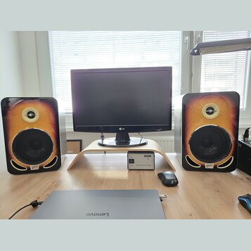 Dva studiové monitory s dřevěným provedením v přechodové barvě od žluté po tmavě hnědou. Na spodní části každého reproduktoru je viditelné logo Gibso…