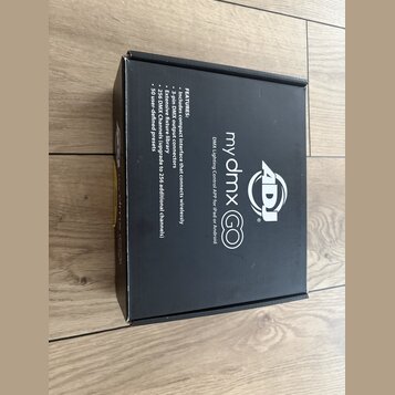 Černá papírová krabice s bílým textem a logem. Na povrchu je uveden název my dmx GO, popis DMX Lighting Control APP for iPad or Android a logo ADJ. V…