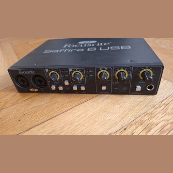 Černý zvukový interface s nápisem Focusrite Saffire 6 USB na horní straně a logem Focusrite vlevo na předním panelu. Přední strana obsahuje dva kombi…