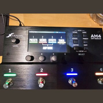 Černý kytarový procesor s nápisem FRACTAL AUDIO SYSTEMS a označením AM4 AMP MODELER. Zařízení má digitální displej, který zobrazuje menu s položkami…