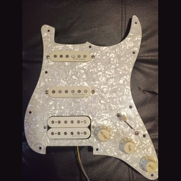 Bílý pickguard s perleťovým efektem osazený třemi snímači. Na dvou horních snímačích je nápis „R.M. pickups“, na spodním humbuckeru je částečně vidit…