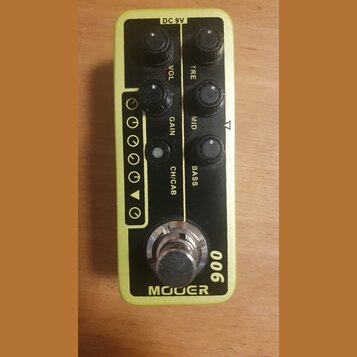 Žlutý kytarový efekt s černým horním panelem. Na panelu je nápis MOOER a číslo 006, dále popisky ovládacích prvků GAIN, VOL, BASS, MID a TRE s nápise…