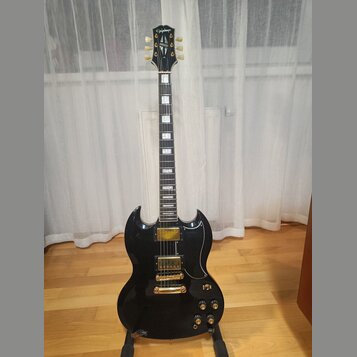 Černá elektrická kytara s dvojstupňovitým tělem a hnědým hmatníkem s trapezoidními vložkami. Na hlavě je bílý nápis Epiphone a zlaté loga. Nástroj má…