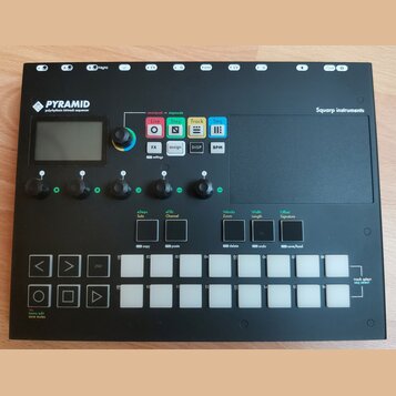Černý sekvencer s nápisem PYRAMID polyrhythmic 64track sequencer a značkou Squarp instruments. Zařízení obsahuje displej, pět otočných ovladačů, něko…