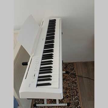 Bílé digitální piano na bílém stojanu s otevřeným krytem klávesnice. Na levé straně je nápis ES110 a na horní hraně těla nápis KAWAI. Nástroj vykazuj…