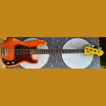 Oranžová elektrická basová kytara s červeným perleťovým pickguardem. Na hlavě hmatníku je nápis Vintage ICON Series. Povrch těla vykazuje výrazné odř…