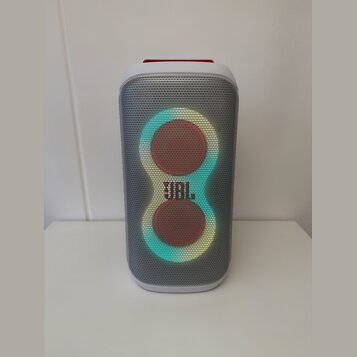 Bílý přenosný reproduktor s šedou kovovou mřížkou. Uprostřed je umístěno podsvícené logo JBL a dvě kulaté svítící plochy. Horní část reproduktoru je…