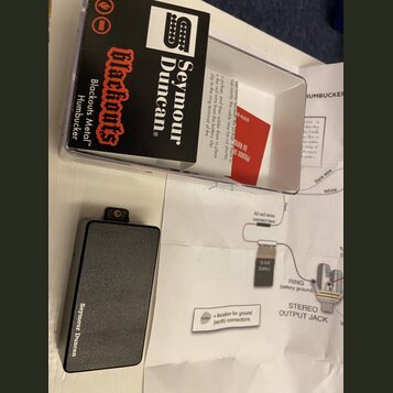 Na fotografii je černý obdélníkový modul s nápisem Seymour Duncan a doprovodný papírový návod se schématem zapojení. Modul je umístěn vedle průhledné…