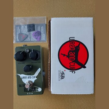 Kytarový efekt v olivově zeleném provedení s nápisy VOLUME, DISTORTION a TONE. Na spodní části je bílé logo s nápisem WREN and CUFF, pod ním text TAL…