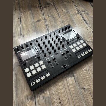 Černý DJ kontrolér s nápisem TRAKTOR KONTROL S5. Zařízení obsahuje několik faderů, zahlreichen otočných knoflíků a dvě sady bílých čtvercových podsví…