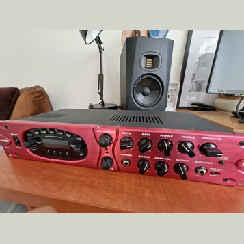 Červený kytarový zesilovač s černým horním krytem. Na předním panelu jsou nápisy POWER, AMP MODELS, DRIVE, BASS, MIDDLE, TREBLE a PRESENCE. V levé čá…