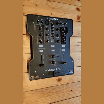 Černý DJ mixér značky ALLEN&HEATH, model Xone:23C. Na předním panelu jsou umístěny knofíky, posuvníky a tlačítka s nápisy jako MIX, MASTER, MONITOR,…