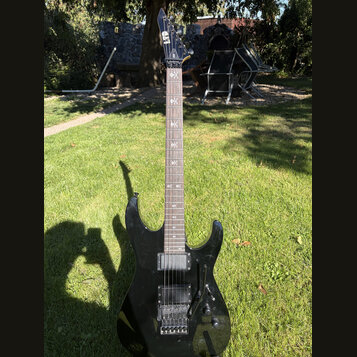 Černá elektrická kytara s ostře zakončenou hlavou a dvěma humbuckery. Na hlavě je bílé logo LTD, na hředníku jsou vložky s křížovými symboly. Tělo i…