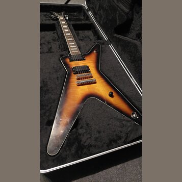 Elektrická kytara s tělem ve tvaru Flying V v barevné variantě sunburst, umístěná v černém tvrdém kufru. Nástroj má dva humbuckery, dva ovládací knof…