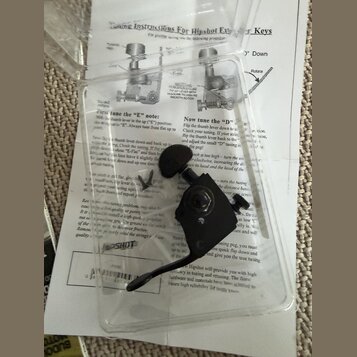 V plastovém obalu se nachází černý ladicí klíč z kovu. Pod ním je viditelný papírový návod s nadpisem Tuning Instructions For Hipshot Extender Keys a…
