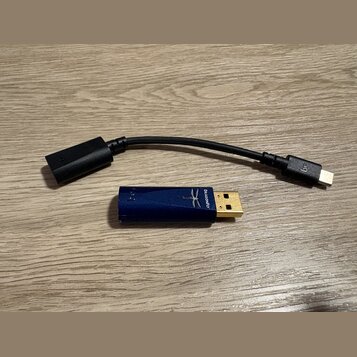 Na fotografii je modrý USB dongle s logem vály a nápisem DRAGONFLY. Vedle něj leží černý adaptér s kabelem, který má na jednom konci USB-C konektor a…