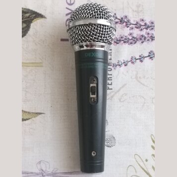 Černý dynamický mikrofon s kovovou stříbrnou mřížkou. Na horní části těla je bílý nápis DEXON a pod ním drobným písmem text ELECTRODYNAMIC MICROPHONE…