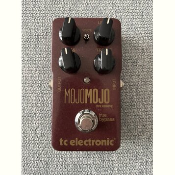Bordeaux červený efekt pedál s nápisy MOJOMOJO a OVERDRIVE. Na spodní části je logo tc electronic a text true bypass. Pedál má čtyři černé ovládací k…