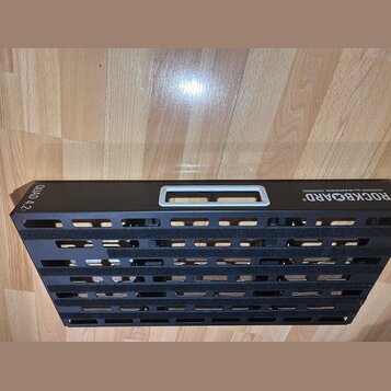Černý kovový pedalboard s vodorovnými otvory a úchytkou. Na povrchu jsou bílé nápisy ROCKBOARD®, BY WARWICK a QUAD 4.2. Povrch je v dobrém stavu, bez…
