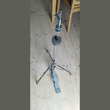 Stříbrný kovový stojan na činely s trojnožkou. Na pedálu je vidět logo "Remo" a nápis "SOUND-LINE". Povrch kovových částí vykazuje známky běžného opo…