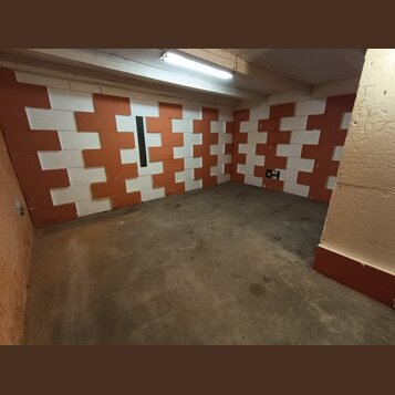 Fotografie zachycuje interiér místnosti s betonovou podlahou. Stěny jsou vyloženy akustickými panely v červenohnědé a bílé barvě, uspořádanými do šac…