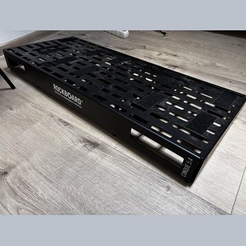 Černý kovový pedalboard s perforovaným povrchem a bočními úchopy. Na boku je bílý nápis ROCKBOARD by WARWICK a v pravém dolním rohu označení CINQUE 5…