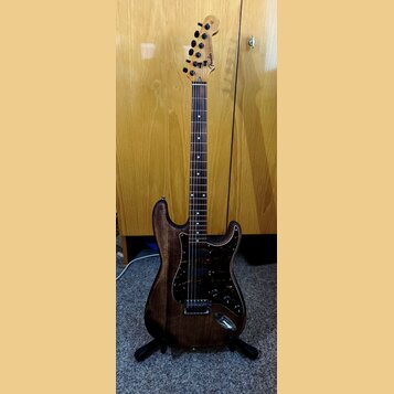 Elektrická kytara s tmavě hnědým dřevěným korpusem a hnedým hmatníkem. Kytara má tmavý vzorovaný pickguard a na hlavě je viditelné logo Fender spolu…