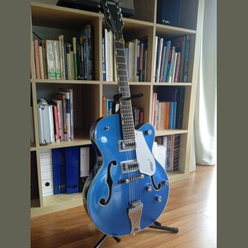 Modrá polodublová elektrická kytara s f-otvory a bílým pickguardem. Na hlavě hрифu je nápis GRETSCH a na pickguardu je viditelné logo GRETSCH. Nástro…