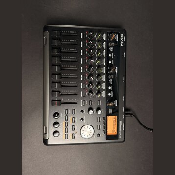 Černý digitální multitrackový nahrávací studiový mixér značky TASCAM, model DP-02. Zařízení obsahuje několik faderů, otočných knoflíků a ovládacích t…