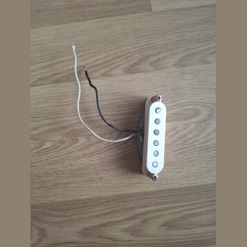 Bílý snímač typu single-coil s pěti viditelnými magnetickými póly. K snímači vedou dva volné vodiče, jeden bílý a jeden černý. Snímač je upevněn dvěm…