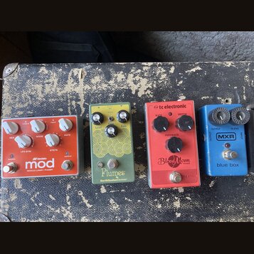 Čtyři efektové pedály v řadě. Horní oranžový pedál nese nápisy „mod“, „MODULAR LUNAR / PHASER“ a logo „M-audio“. Druhý pedál je zelený s žlutým ornam…