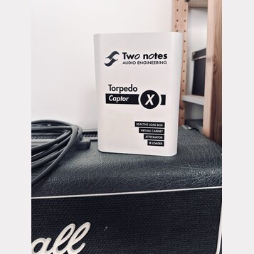 Bílý hranatý přístroj s nápisy Two notes AUDIO ENGINEERING a Torpedo Captor X. Dole jsou uvedeny funkce REACTIVE LOAD BOX, VIRTUAL CABINET, ATTENUATO…