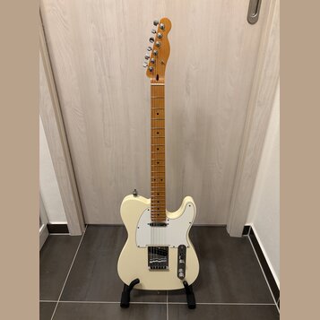Krémová elektrická kytara typu Telecaster s javorovým hnedým hmatníkem a bílým pickguardem. Na hlavě nástroje je viditelné logo Fender. Kytara stojí…