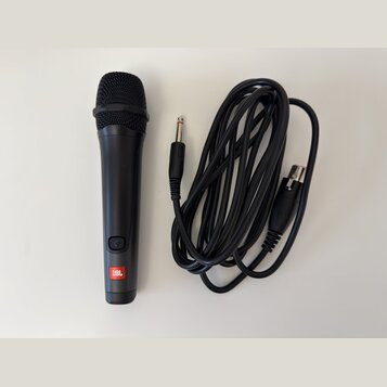Černý dynamický mikrofon s mřížkou a připojeným černým kabelem. Na spodní části mikrofonu je umístěno červeno-bílé logo JBL a nad ním se nachází tlač…