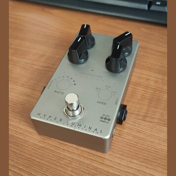 Stříbrný efekt pedál s dvěma černými oválnými knoflíky. Na spodní části je nápis HYPER LUMINAL a pod ním menším písmem HYBRID COMPRESSOR. Na horní čá…