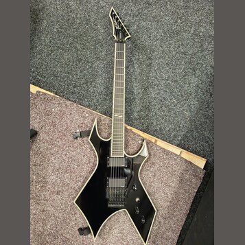 Černá elektrická kytara s ostře hranatým korpusem a bílým lemováním. Na hlavě hmatníku je viditelné logo "Jackson". Nástroj má dva humbuckery, černý…