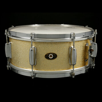Zlatý buben s kovovými obručemi a ladidly. Uprostřed korpusu je oválný štítek s nápisy „Slingerland“, „QUALITY DRUMS“ a „CHICAGO, ILL. U.S.A.“. Povrc…