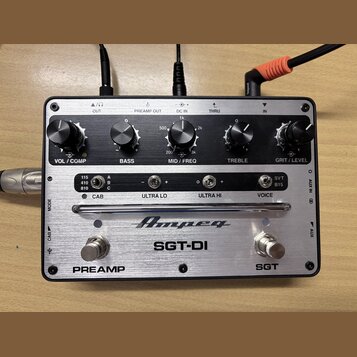 Stříbrný kytarový preamp s nápisem Ampeg a modelem SGT-DI. Zařízení má pět černých otočných ováčků s popisky VOL / COMP, BASS, MID / FREQ, TREBLE a G…