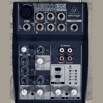 Tmavě šedý mixážní pult s bílými a červenými popisky. Na horní části je nápis XENYX 502, pod ním text PREMIUM 5-INPUT 2-BUS MIXER • XENYX MIC PREAMP…