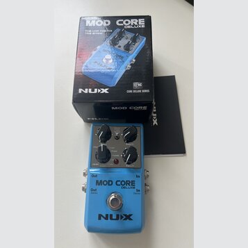 Modulární efekt pedál modrý s nápisy MOD CORE DELUXE a NUX. Na horní části jsou tři černé otočné ovladače s popisky Depth, Tweak a přepínač Deluxe T…